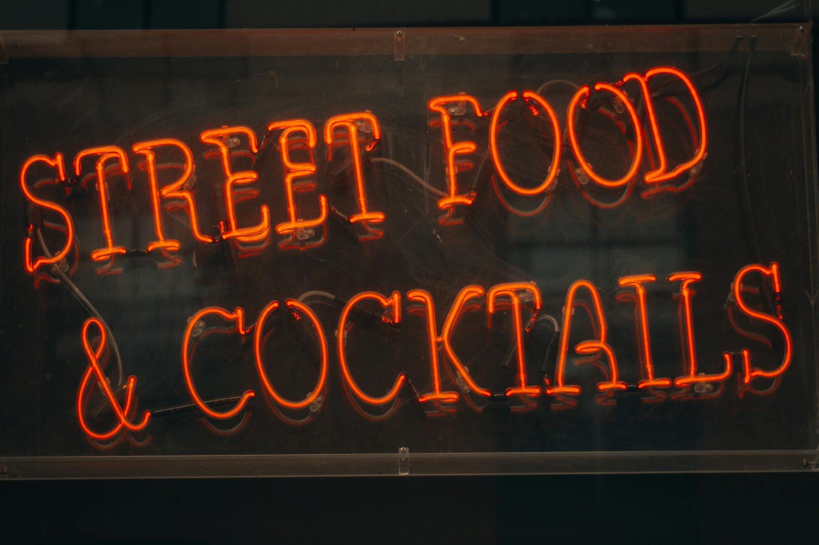 A glowing neon sign advertising street food and cocktails in bright red letters.