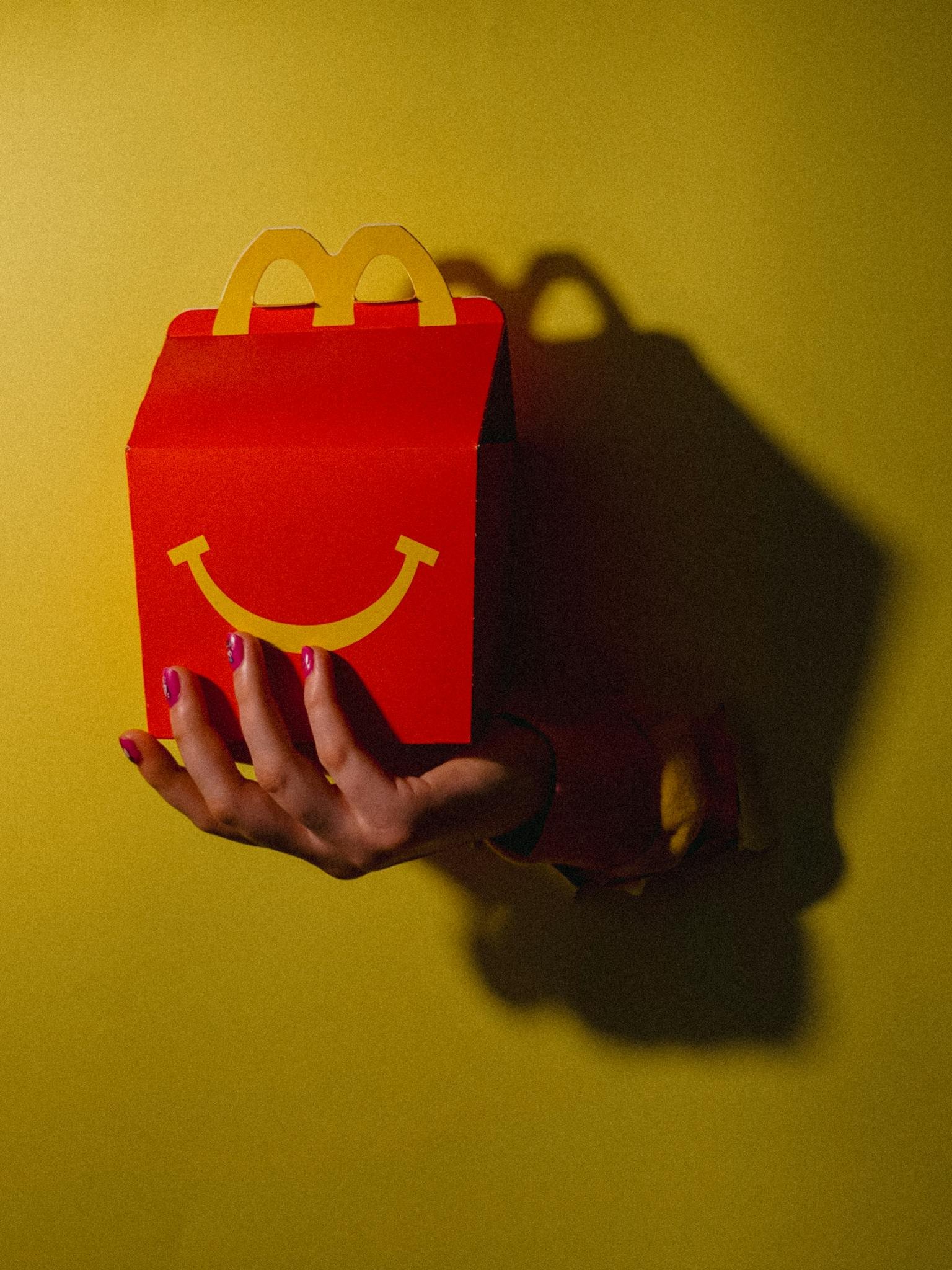 Vibrant shot of a hand holding a red takeout box with a smiley face against a yellow background.